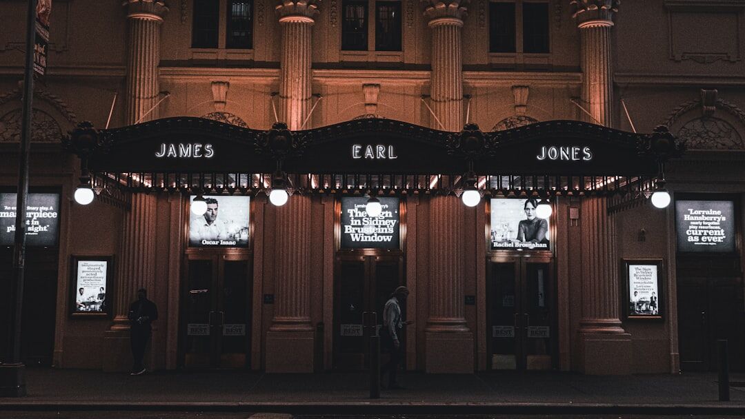 Wide view of an illuminated theater facade at night with guests arriving